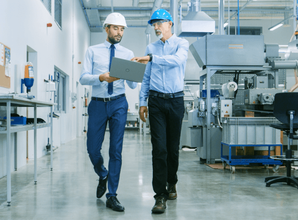 Two people looking at a laptop walking through an industrial facility